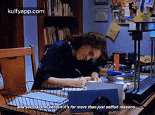 a woman is sitting at a desk writing on a piece of paper while a projector is behind her .