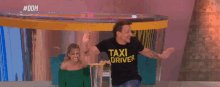 a man in a black shirt with the word driver on it stands in front of a woman