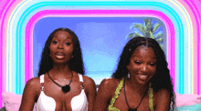 two women are sitting next to each other in front of a rainbow and palm tree .