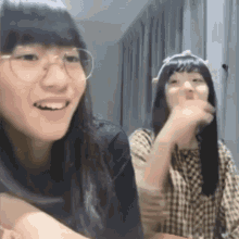 two girls wearing glasses are sitting next to each other and talking .