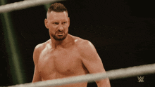 a shirtless wrestler stands in a ring with a w logo on the bottom