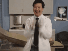 a man in a lab coat and tie is clapping his hands in a hospital room .