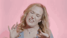 a blonde woman wearing a blue shirt and a necklace is making a funny face