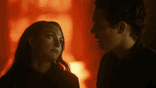 a man and a woman are looking at each other in a dark room with a fire in the background .