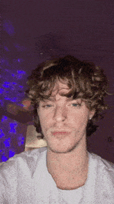 a young man with curly hair is wearing a white shirt and a nose ring