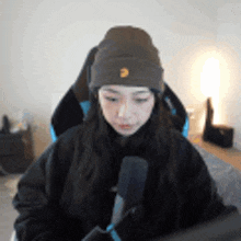 a woman wearing a beanie is sitting in front of a microphone in a room .
