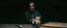 a man is sitting at a table smoking a cigarette and holding a dog