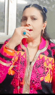 a woman in a pink and black embroidered jacket is holding a string in her mouth