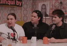 a group of people are sitting at a table with microphones and mugs .