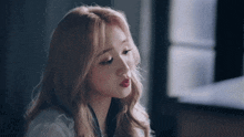a woman with long blonde hair and red lips is sitting in front of a window and looking down .