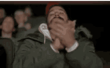 a man with a mustache is covering his mouth with his hands while sitting in a theater .