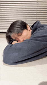a man in a blue hoodie is sleeping with his head on his arm
