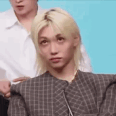 a man with blonde hair is making a funny face while a woman holds his shoulder .
