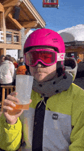 a man wearing a pink uvex helmet and goggles is holding a cup of beer