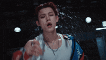 a man in a white tank top is spraying water on his face