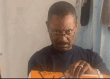 a man wearing glasses and a ring is looking at something in a box .