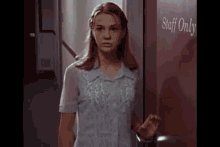 a woman in a blue dress is standing in front of a door that says staff only .