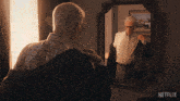 an older man adjusts his jacket in front of a mirror with netflix written on the bottom right