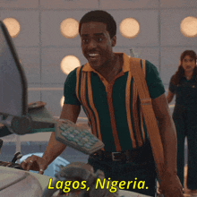 a man in a green and yellow striped shirt is standing in front of a computer and says lagos nigeria