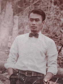 a man wearing a bow tie and a watch stands in front of a wall