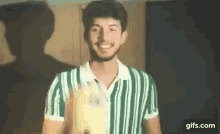 a young man in a green and white striped shirt is smiling and holding a bottle .