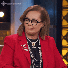a woman wearing glasses and a red jacket is sitting in front of a cb dragonsden logo