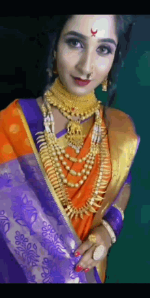 a woman wearing a purple and orange saree and gold jewelry is looking at the camera .