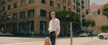 a man in a white shirt with the letter d on his pants stands on a street corner