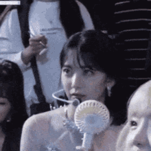 a woman is holding a small fan in her mouth while sitting in a crowd of people .