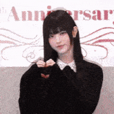 a woman with long black hair is making a heart shape with her hands in front of a sign that says anniversary .