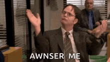 a man in a suit and tie is sitting in an office with his arms in the air and says awnser me .