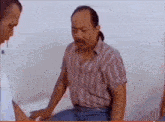 a man in a striped shirt is sitting on a table talking to another man .
