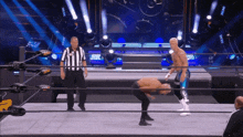 a referee stands behind a wrestler in a wrestling ring while the wrestler performs a trick