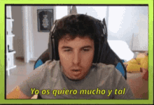 a man wearing headphones is sitting in front of a screen that says yo os quiero mucho y tal .