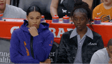a woman wearing a black jacket with the name amiri on it sits next to another woman