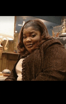 a woman in a brown coat looks at the camera with a lamp in the background