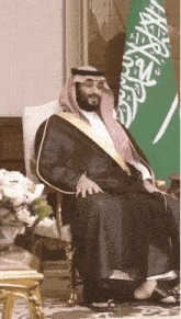 a man sitting in front of a flag with arabic writing on it