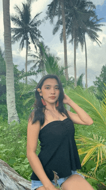 a woman in a black top and shorts is posing for a picture in front of palm trees