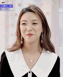 a woman wearing a black and white collared shirt and earrings is smiling
