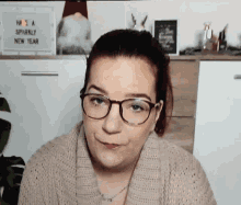 a woman wearing glasses and a sweater is standing in front of a sign that says have a sparkly new year .