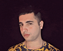 a man wearing a blue and yellow shirt with a gold chain around his neck is looking at the camera .
