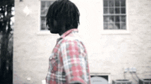 a man in a plaid shirt is standing in front of a brick wall .