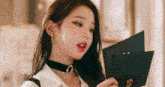 a close up of a woman wearing a choker holding a piece of paper .