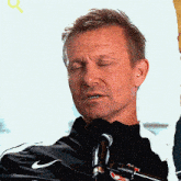 a man wearing a black nike jacket stands in front of a microphone