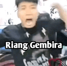 a man is making a funny face while wearing a hat and a t-shirt with the words riang gembira .
