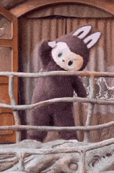 a stuffed animal in a bunny costume stands behind a fence