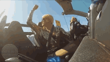 a woman sitting in a car with her fist in the air behind a sign that says no smoking