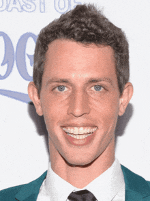 a man wearing a white shirt and a blue jacket smiles for the camera