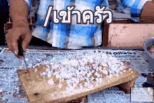 a person in a blue plaid shirt is cutting a piece of cake on a wooden board