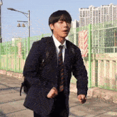 a man in a suit and tie is standing in front of a fence with a sign that says ' warning ' on it